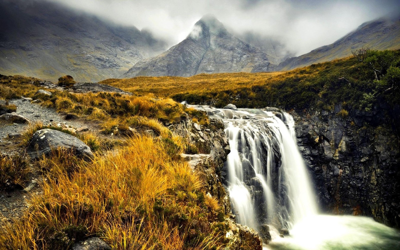 Um close de uma cachoeira em uma área gramada com uma montanha ao fundo. (terras altas da escócia, montanha, cachoeira, natureza, terras altas)