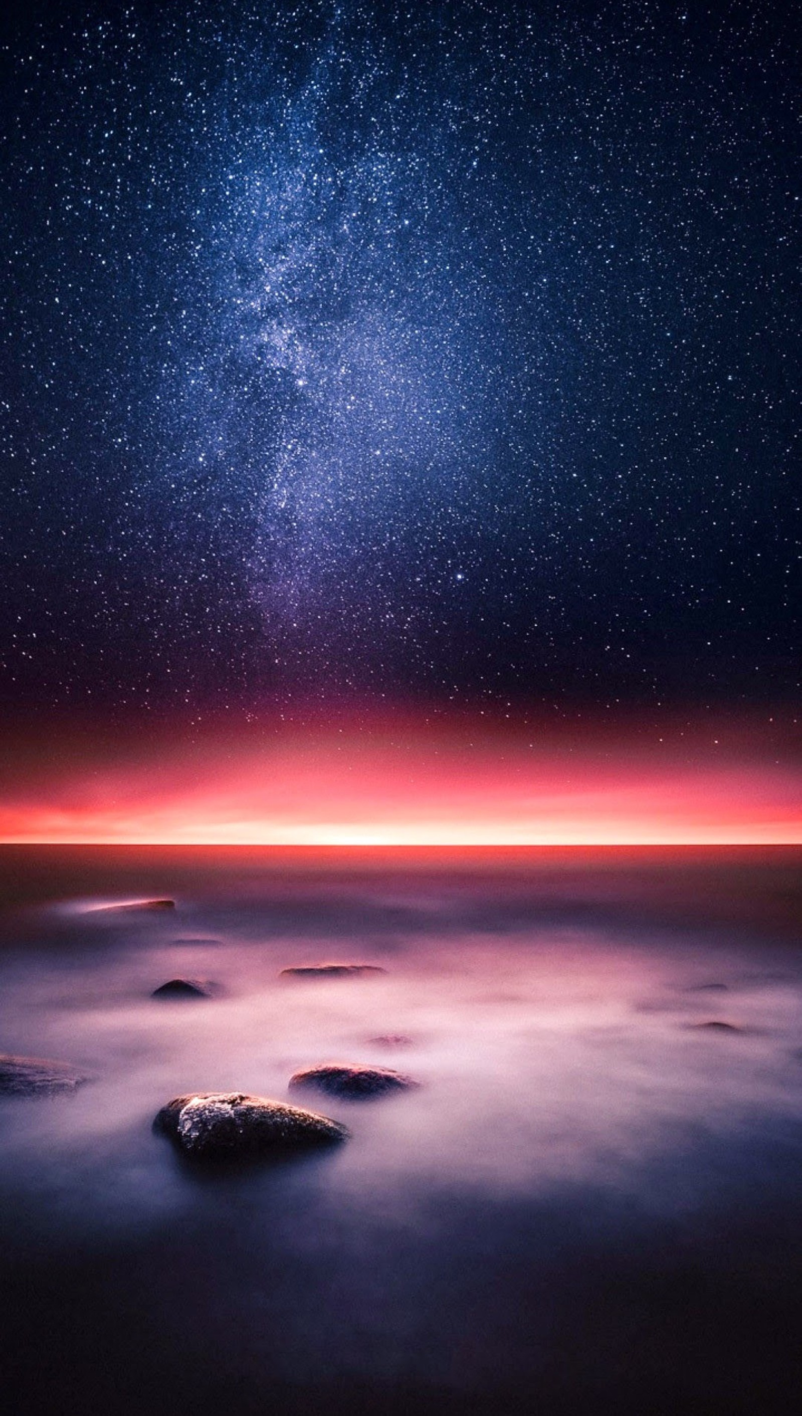 Starry night sky over the ocean with rocks and a bright pink glow (red, rock, sky, space)