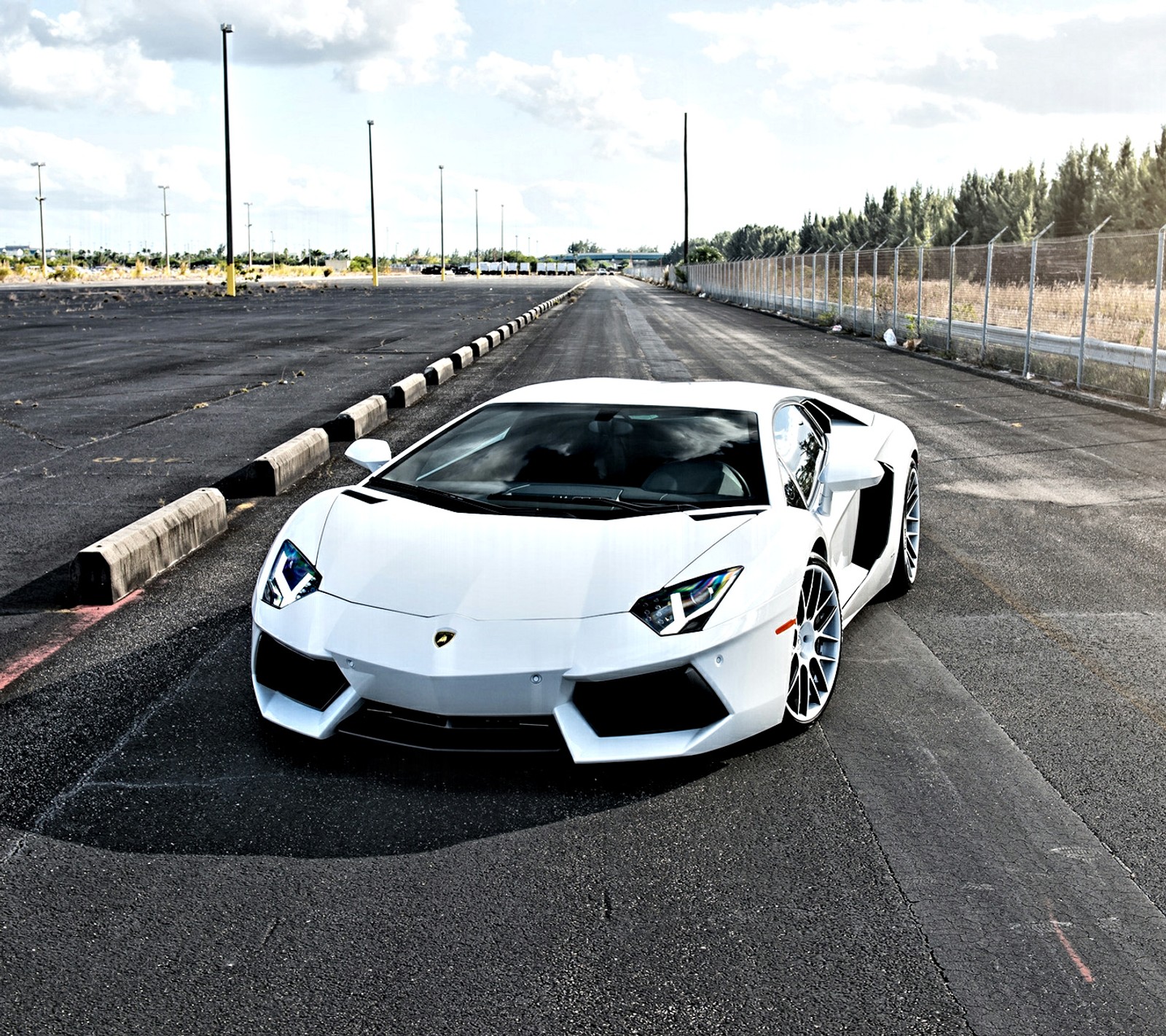 Une voiture de sport arabe blanche garée sur une route avec une clôture en arrière-plan (lambo, lamborghini, supersportive, blanc)