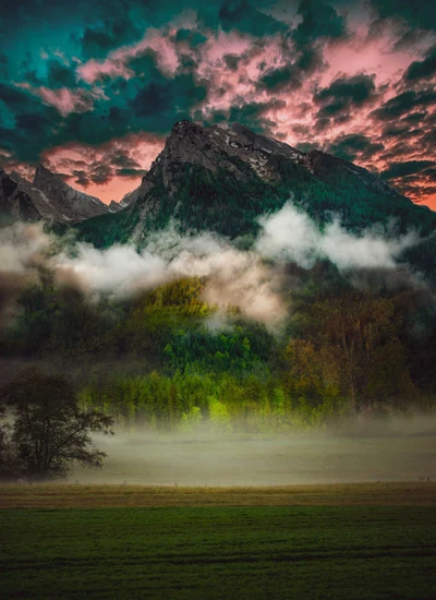 Montanhas majestosas sob um céu colorido em meio a uma vegetação nevoenta