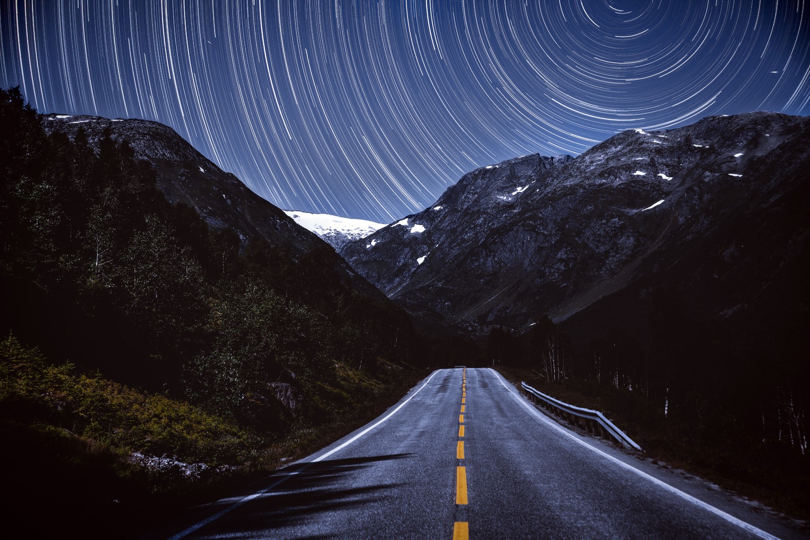 Uma vista de uma estrada com uma trilha de estrelas no céu (montanhas, rastro de estrelas, estrada, tarmac, noite)