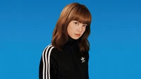 Lisa from BLACKPINK in an Adidas tracksuit against a vibrant blue background.