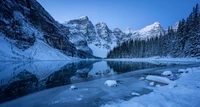 Montanhas cobertas de neve se refletem nas águas serenas do Lago Moraine, cercadas por exuberantes árvores perenes, capturando a tranquilidade da natureza selvagem de inverno do Parque Nacional de Banff.