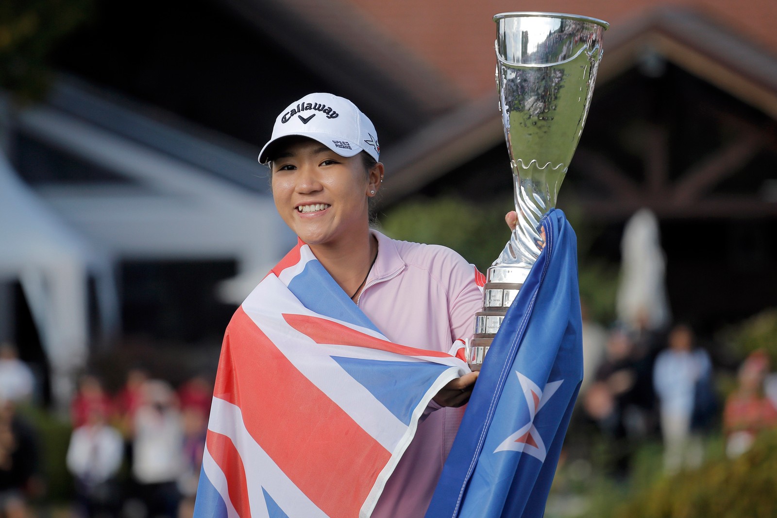 Uma mulher segurando um troféu e uma bandeira com uma multidão ao fundo (golfe, evento de competição, campeonato, torneio, campeonatos)