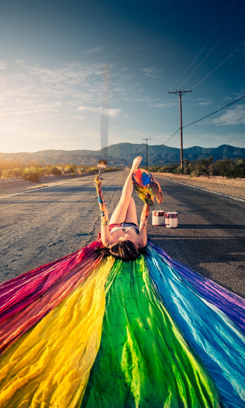 Una mujer árabe acostada en la carretera con una manta de colores del arcoíris (hermoso, azul, femenino, verde, estilo de vida)