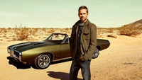 Paul Walker posando ao lado de um carro conversível vintage em uma paisagem desértica.