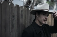 A distinguished male actor in a fedora, posed against a wooden fence, exuding a classic western charm in a black and white setting.