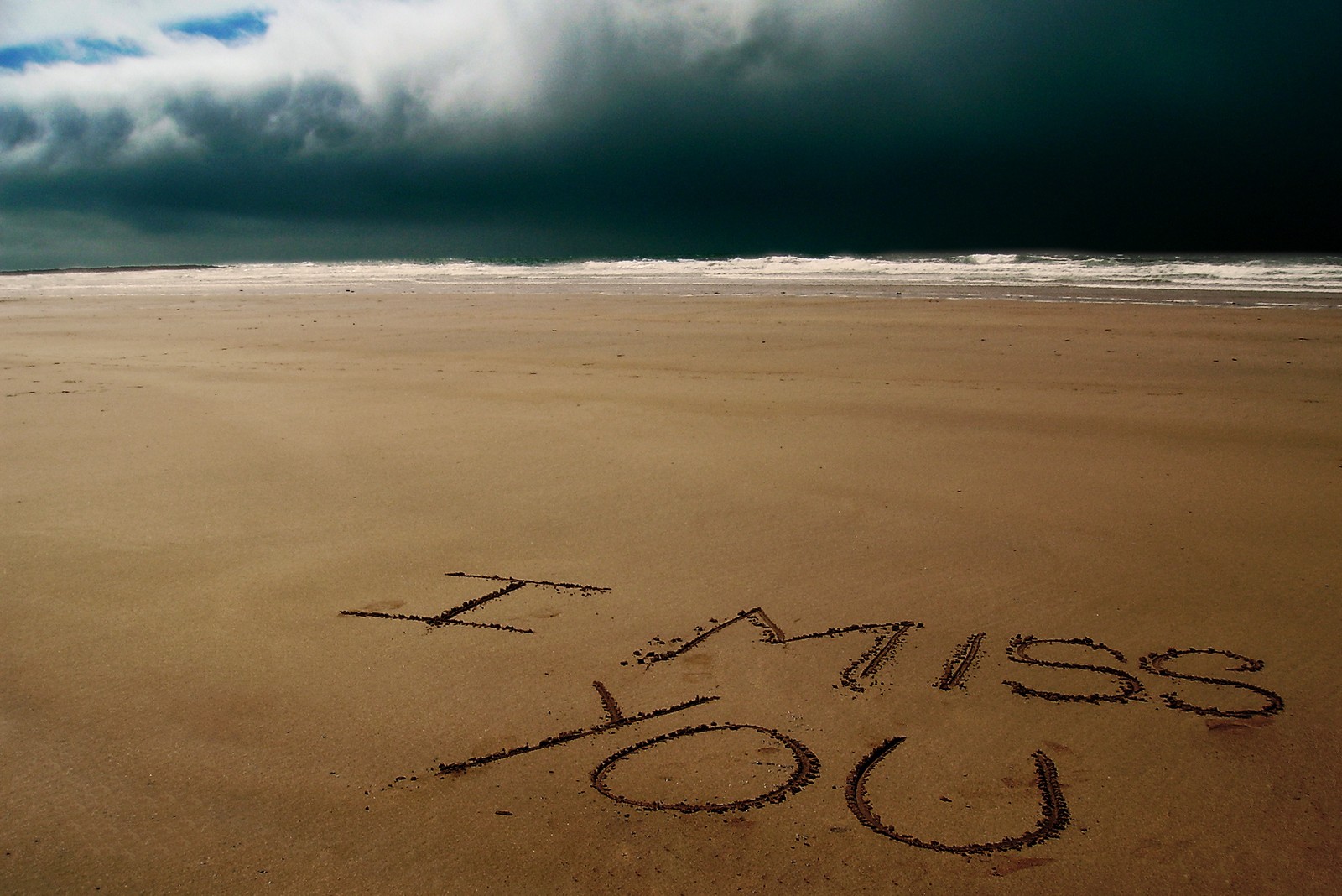 Eine nachricht im sand geschrieben an einem strand mit einem stürmischen himmel (strand, wolke, fräulein, vermisst, ozean)