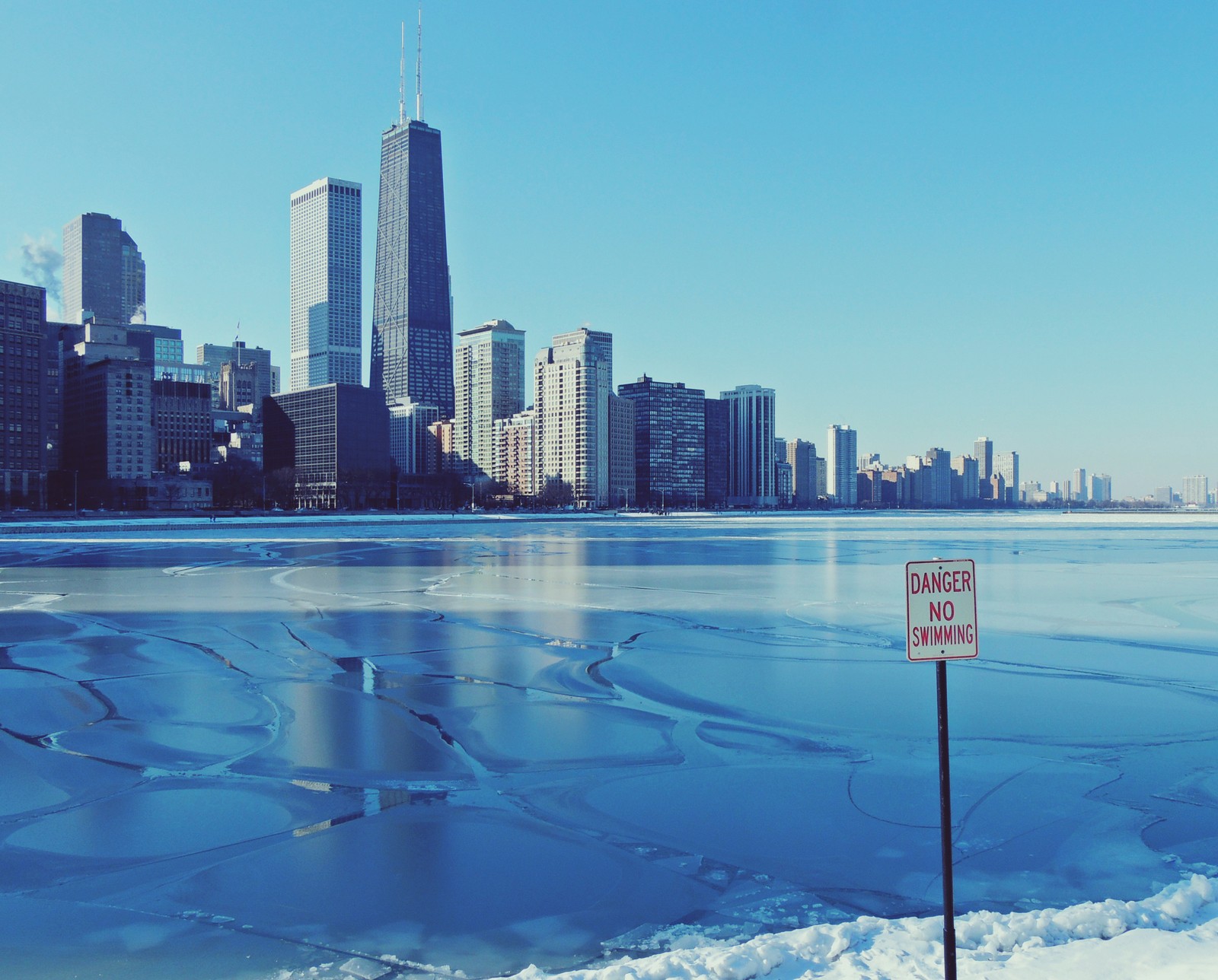 Um lago nevado com gelo e uma placa em frente a um horizonte urbano (chicago, linha do horizonte, cidade, dia, paisagem urbana)