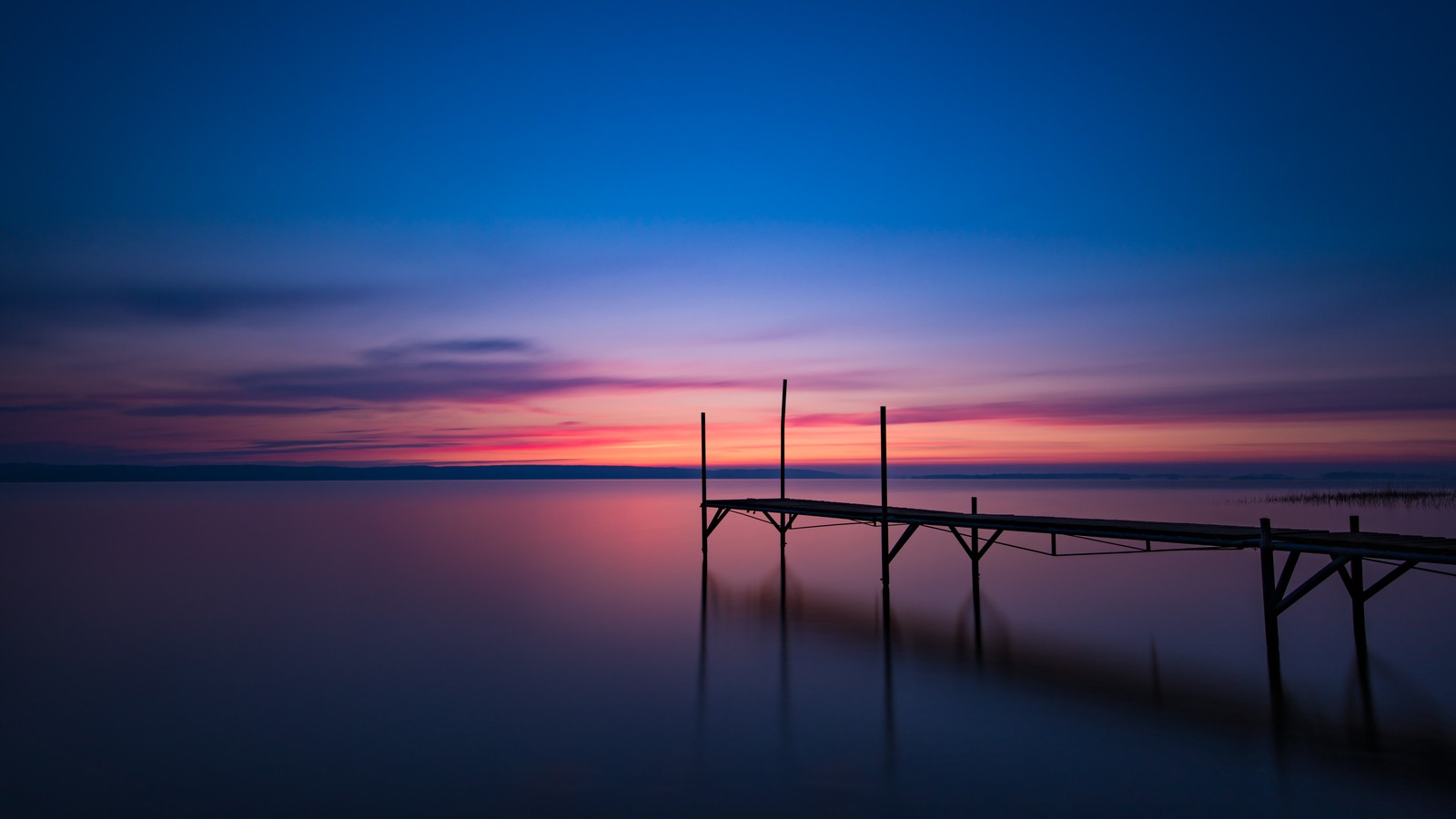 A view of a dock with a boat on the water at sunset (dawn, sunrise, early morning, sweden, roxen lake)