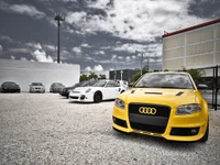 Voiture Audi jaune affichée de manière proéminente dans un parking aux côtés de divers autres véhicules.