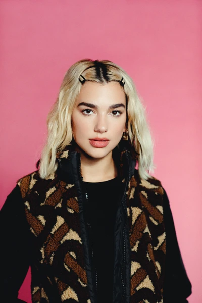 Dua Lipa with a pastel pink background, showcasing her stylish look and disco pop vibe.