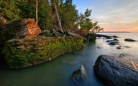 Rive sereine au coucher du soleil avec des reflets et des rochers moussus