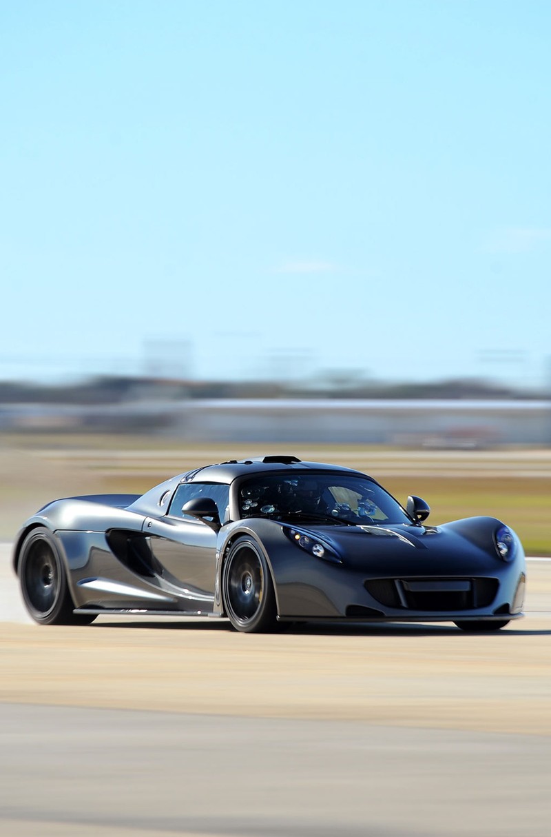 Um carro esportivo preto dirigindo em uma pista com um fundo borrado (gt, venom)