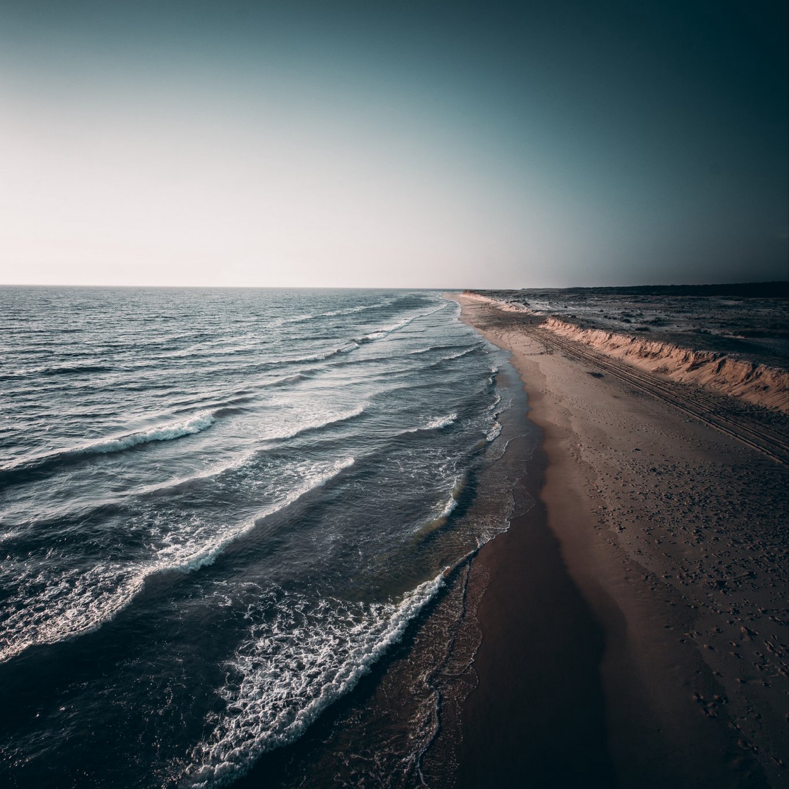 A view of a beach with waves coming in to the shore (wind wave, shore, sky, sea, body of water)