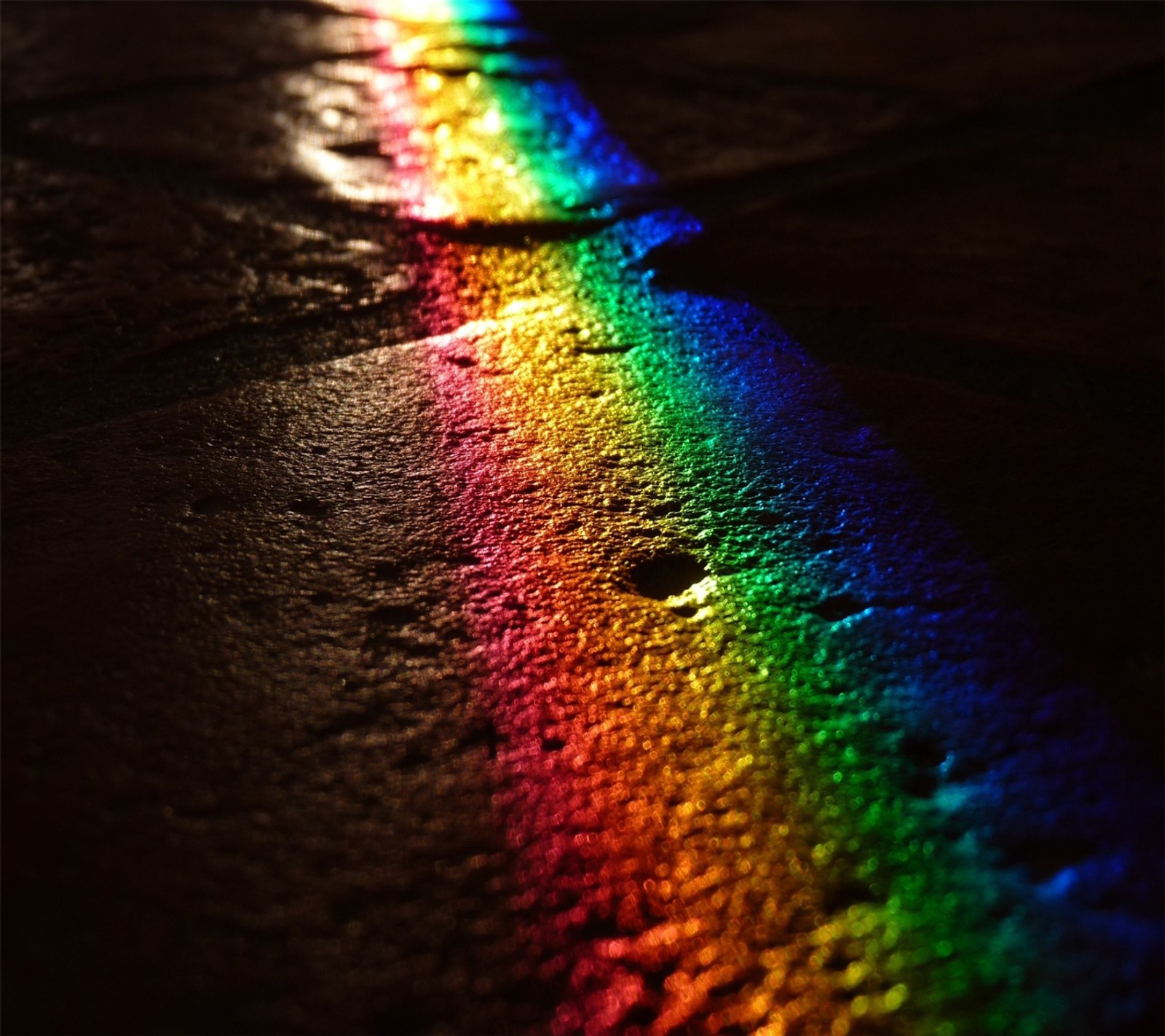 A close up of a rainbow colored light shining on a sidewalk (green, red)