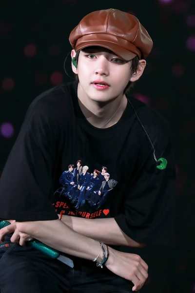 BTS V avec une casquette marron et un t-shirt graphique, dégageant du charisme sur scène.