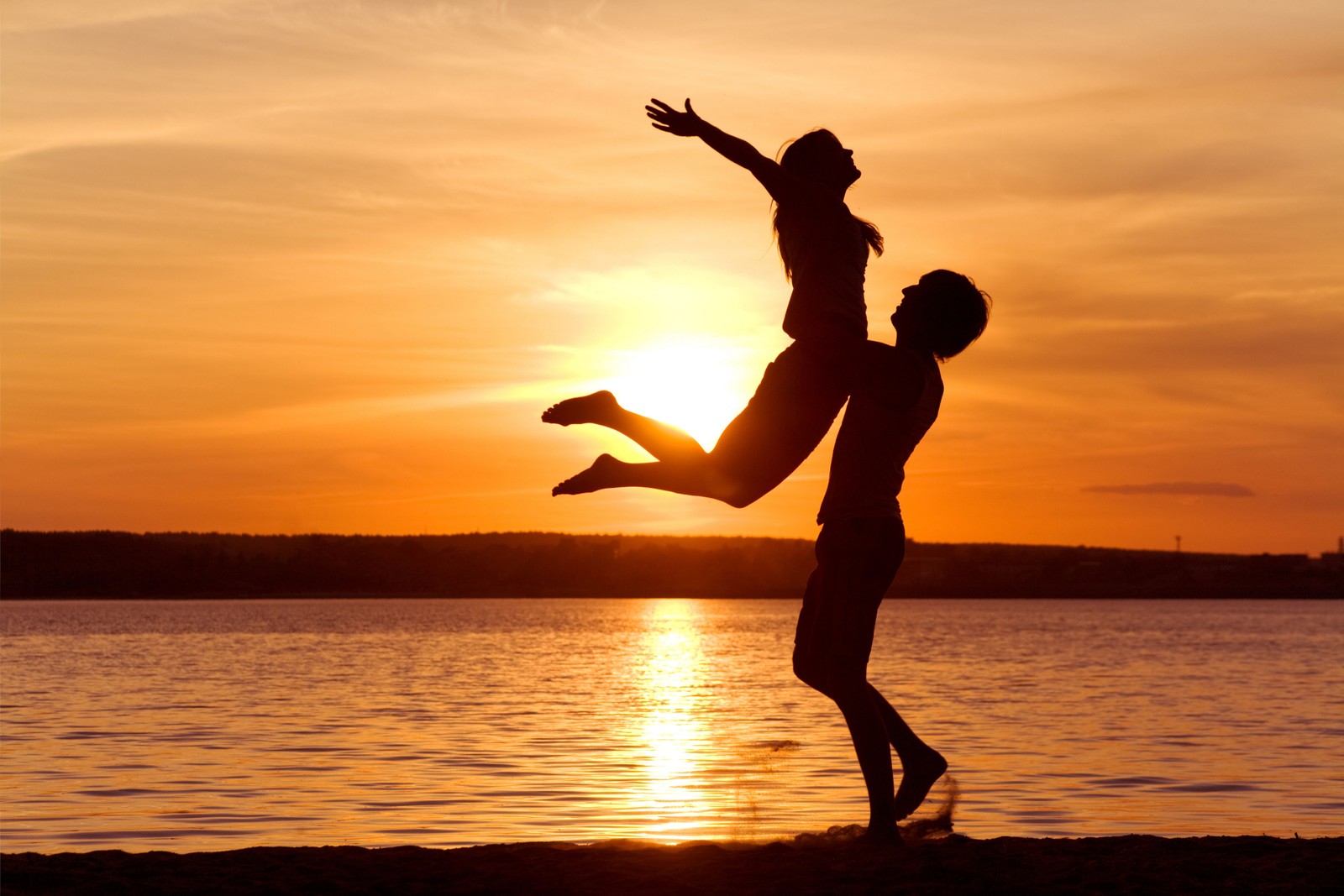 Silhouette d'un homme et d'une femme jouant ensemble sur la plage (romance, eau, coucher de soleil, amusement, sauter)