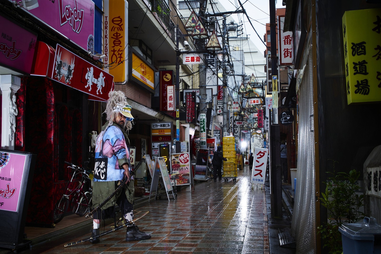 There is a man walking down a street with a skateboard (street, town, alley, urban area, pedestrian)