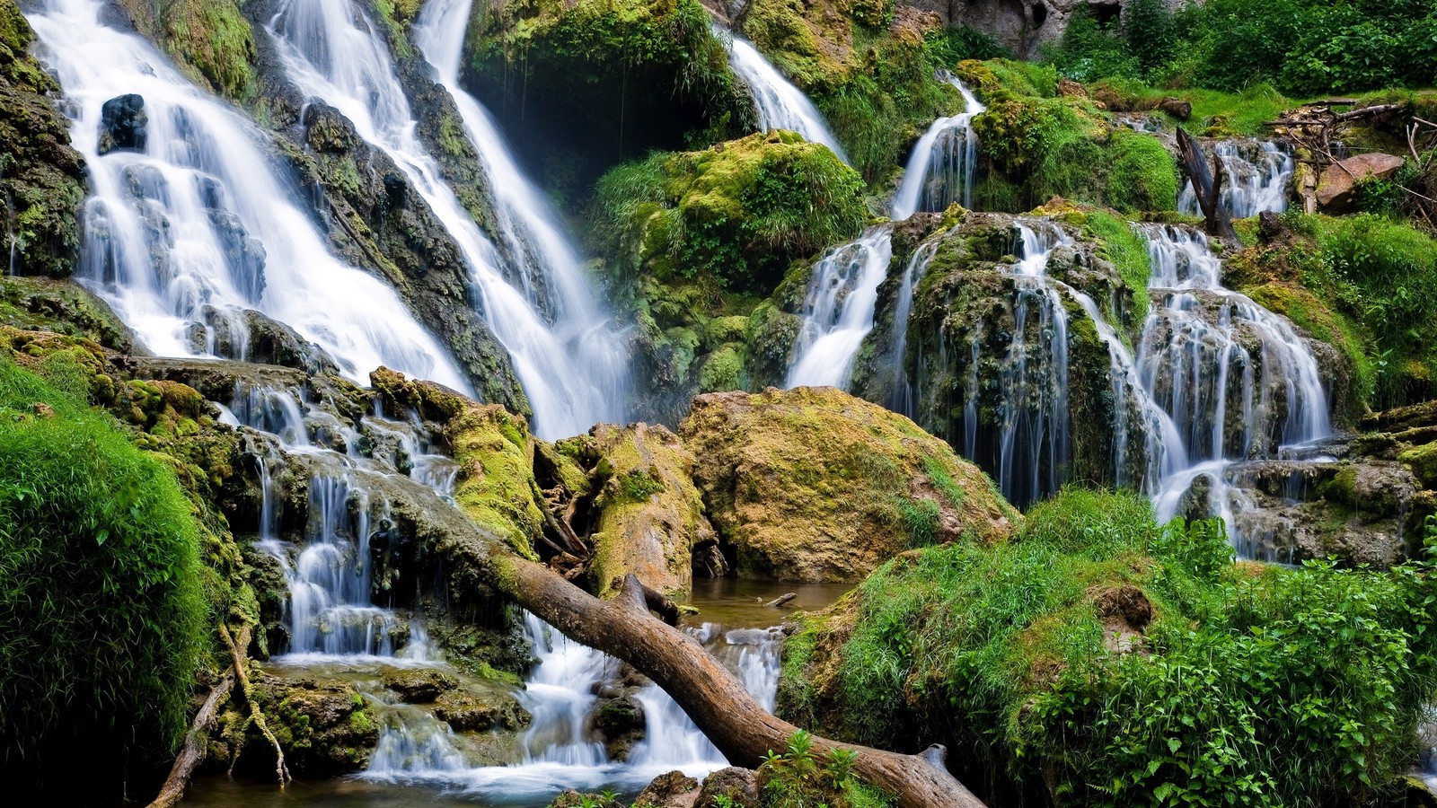 Una gran cascada cayendo por una colina rocosa con árboles (cascada, recursos hídricos, cuerpo de agua, naturaleza, agua)