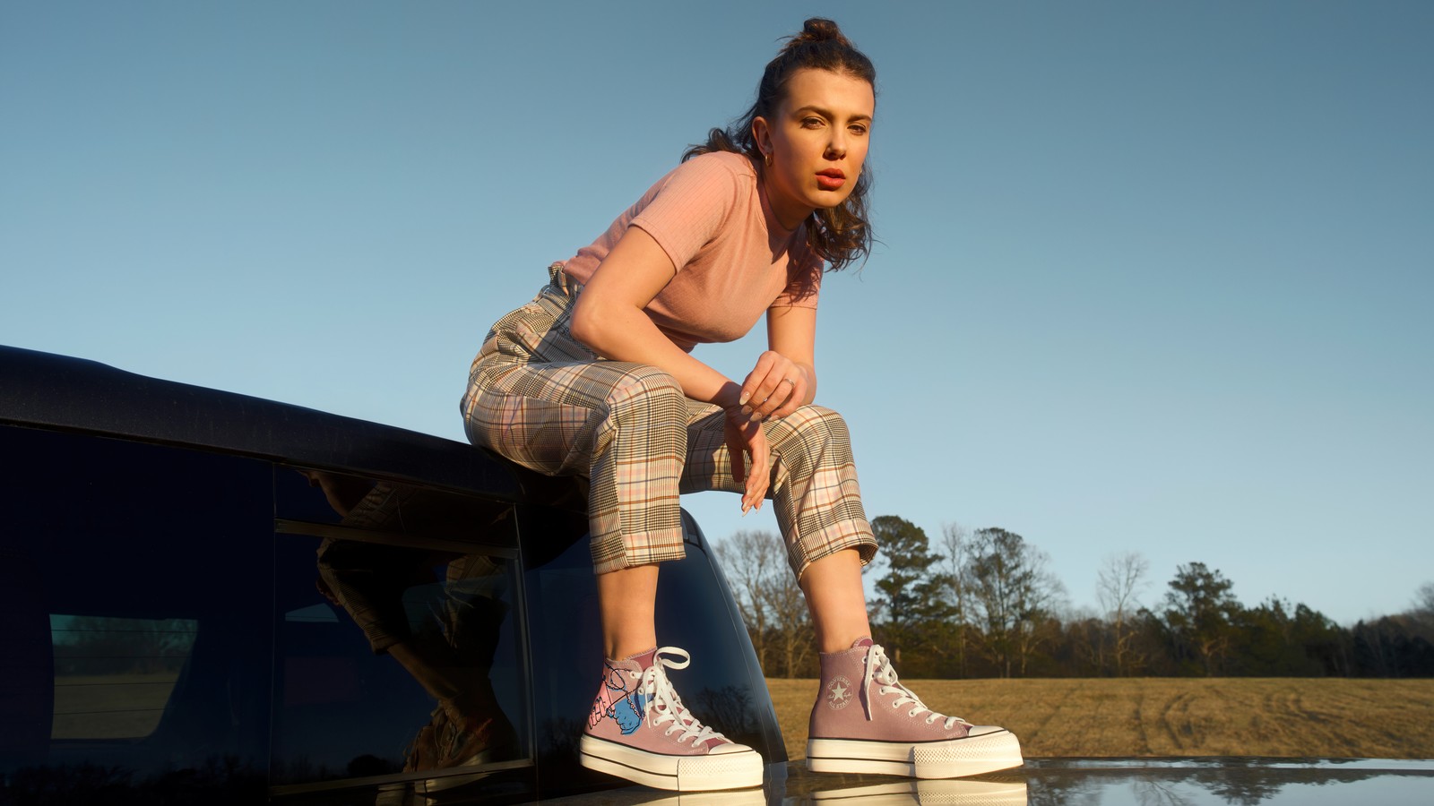 Femme assise sur le toit d'une voiture avec un lac en arrière-plan (millie bobby brown, britannique, actrice, célébrité, filles)