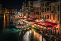 Serenidad nocturna en el Gran Canal: un paisaje urbano reflejado con góndolas y cafés iluminados