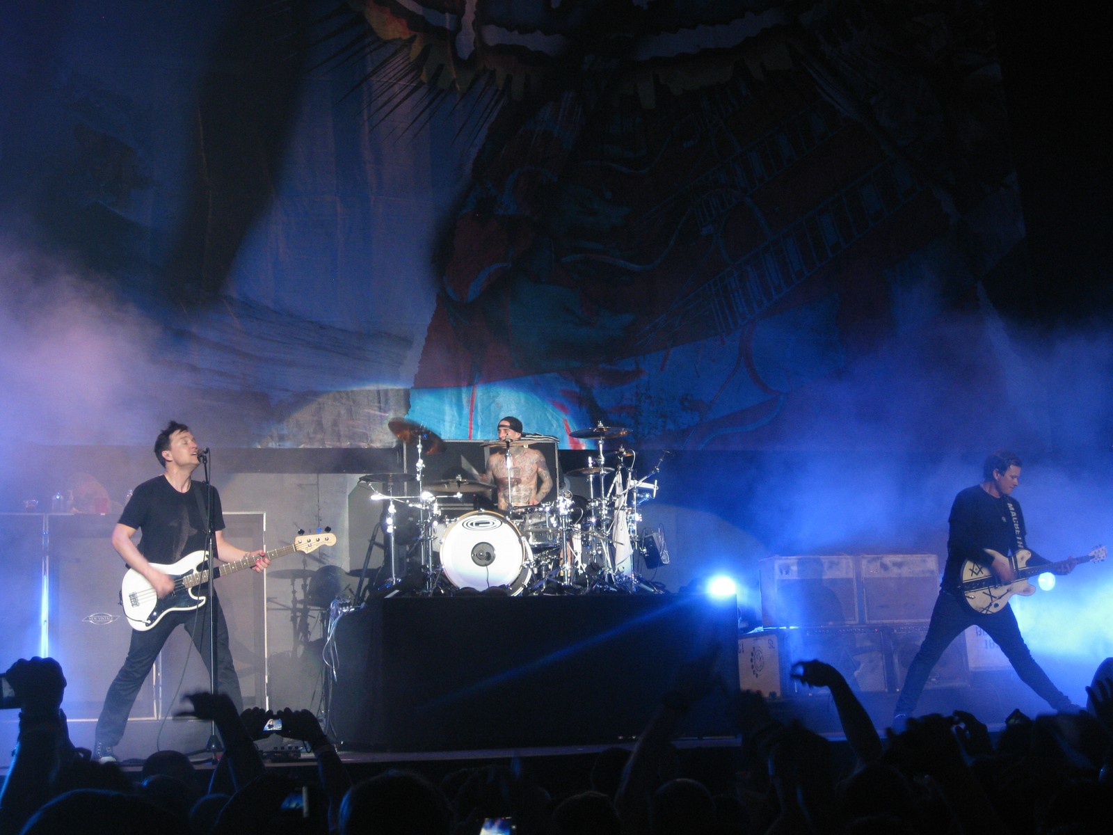 Imagen borrosa de una banda actuando en el escenario con humo saliendo del escenario (blink 182, punk rock, pop punk, parpadeo, conjunto musical)