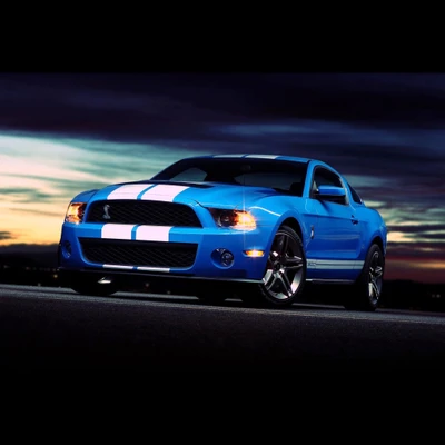 Blauer Ford Mustang Shelby GT500 auf einer malerischen Straße während des Sonnenuntergangs.