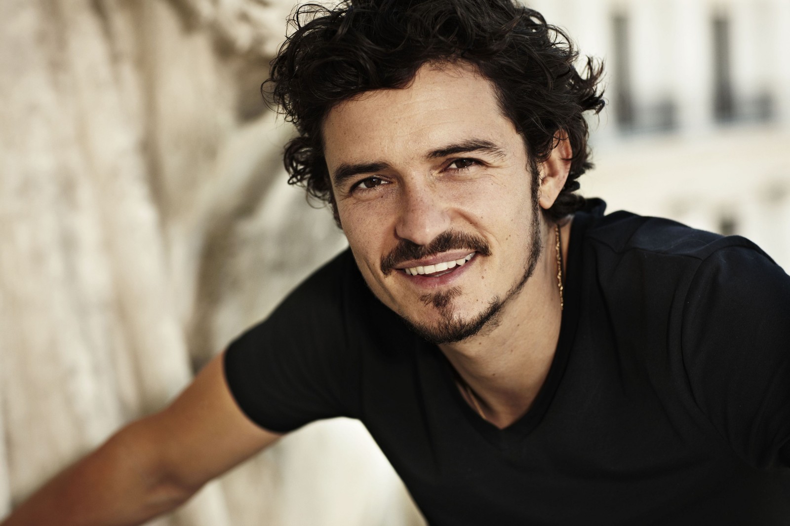 Ein arafed-mann mit lockigen haaren und einem schwarzen hemd lächelt (orlando bloom, haar, gesichtsbehaarung, frisur, kinn)