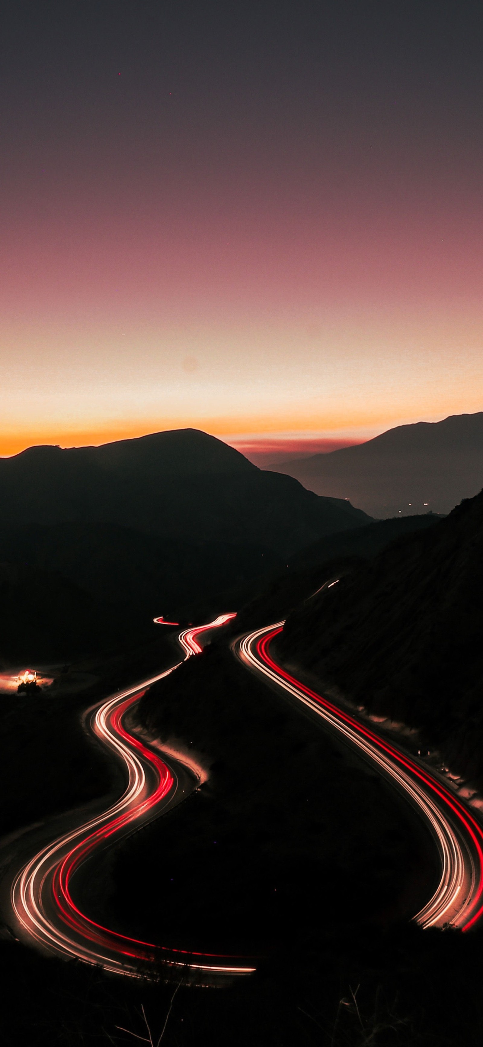 Vista aérea de una carretera sinuosa con un atardecer de fondo (canción, letras, 2021, montaña, superficie de la carretera)