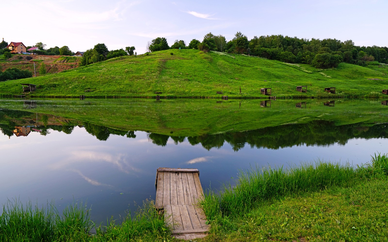 There is a small wooden dock sitting on the bank of a lake (nature, reflection, water, grassland, grass)