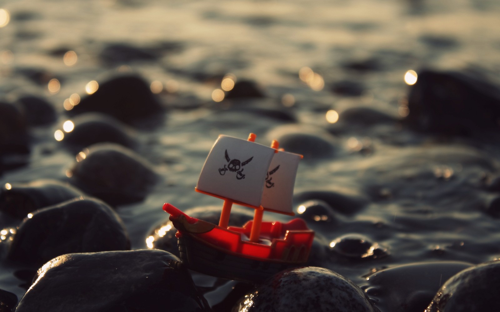 There is a small boat that is sitting on some rocks (water, red, sea, nature, sunlight)