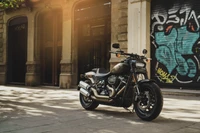 Harley Davidson Fat Bob dans un cadre urbain ensoleillé avec un fond de graffiti