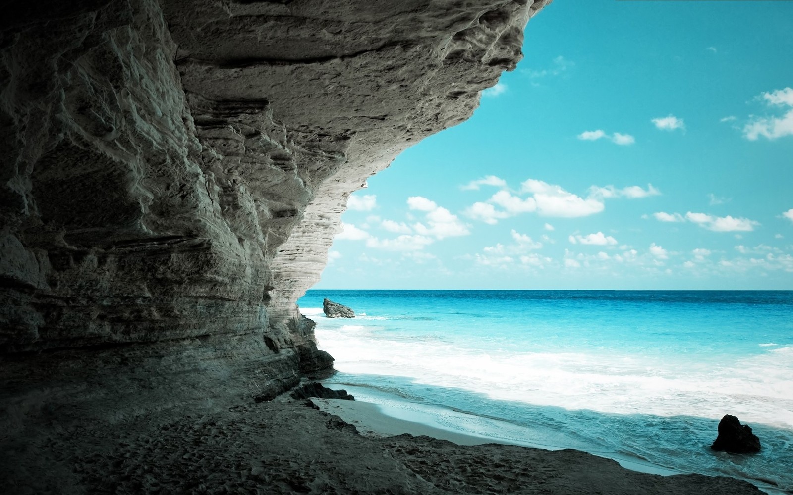 There is a person sitting on the beach looking out at the ocean (sea, ocean, coast, rock, sea cave)