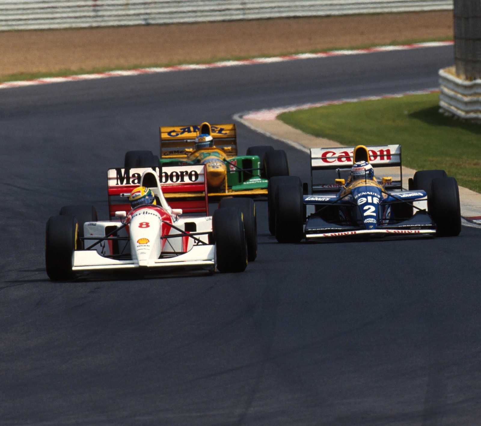 Dos coches de carreras compiten en una pista de carreras con un área de césped verde (benetton, mclaren, prost, schumacher, senna)