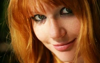 Portrait of a young woman with vibrant red hair, striking green eyes, and subtle freckles on her cheeks.