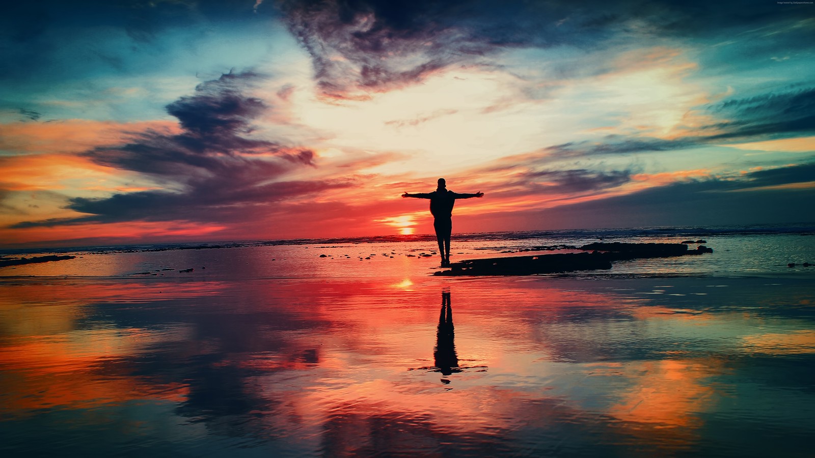 Un homme arabe debout sur la plage les bras écartés (mer, coucher de soleil, réflexion, horizon, paysage)