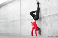 Chica haciendo un pino contra una pared de concreto