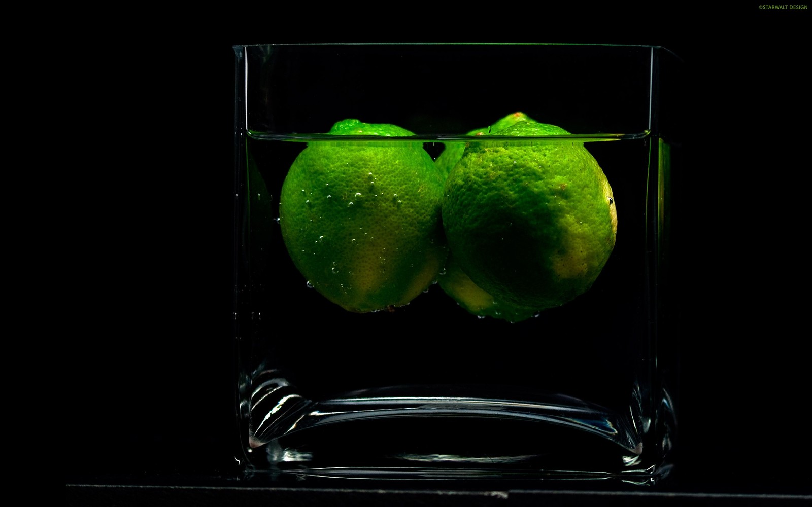 There are two limes in a glass of water with a black background (green, glass, still life, still life photography)