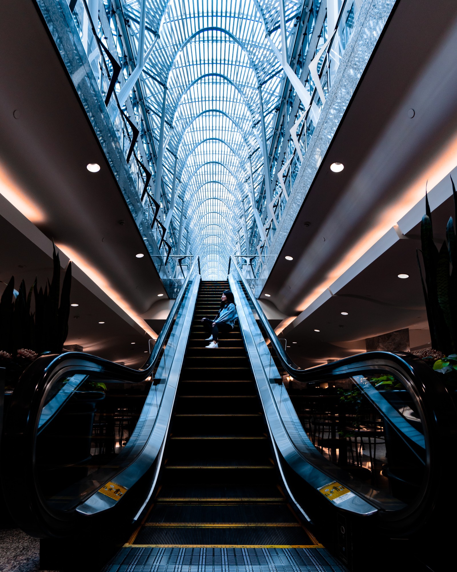 Il y a un homme descendant un escalier roulant dans un bâtiment (ciel, symétrie, ligne, escalier roulant, design)