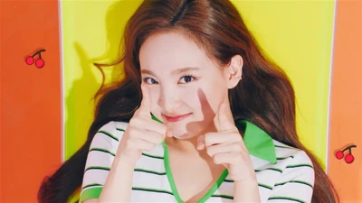 Nayeon von TWICE posiert verspielt mit Fingerpistolen vor einem lebhaften, bunten Hintergrund.