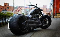 Harley Davidson Softail personalizado com um pneu traseiro largo, estacionado em uma rua da cidade.