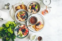 A vibrant spread of healthy breakfast dishes featuring smoothie bowls topped with fresh berries, a plate of waffles adorned with fruit, and a cup of coffee, all set against a marble backdrop.