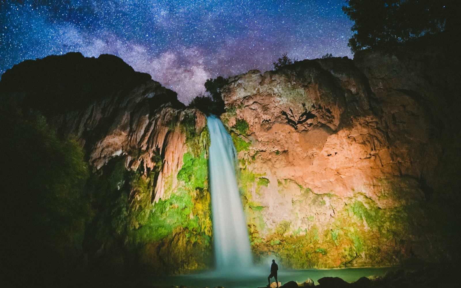 A man standing in front of a waterfall under a night sky (milky way, nature, water, formation, landscape)