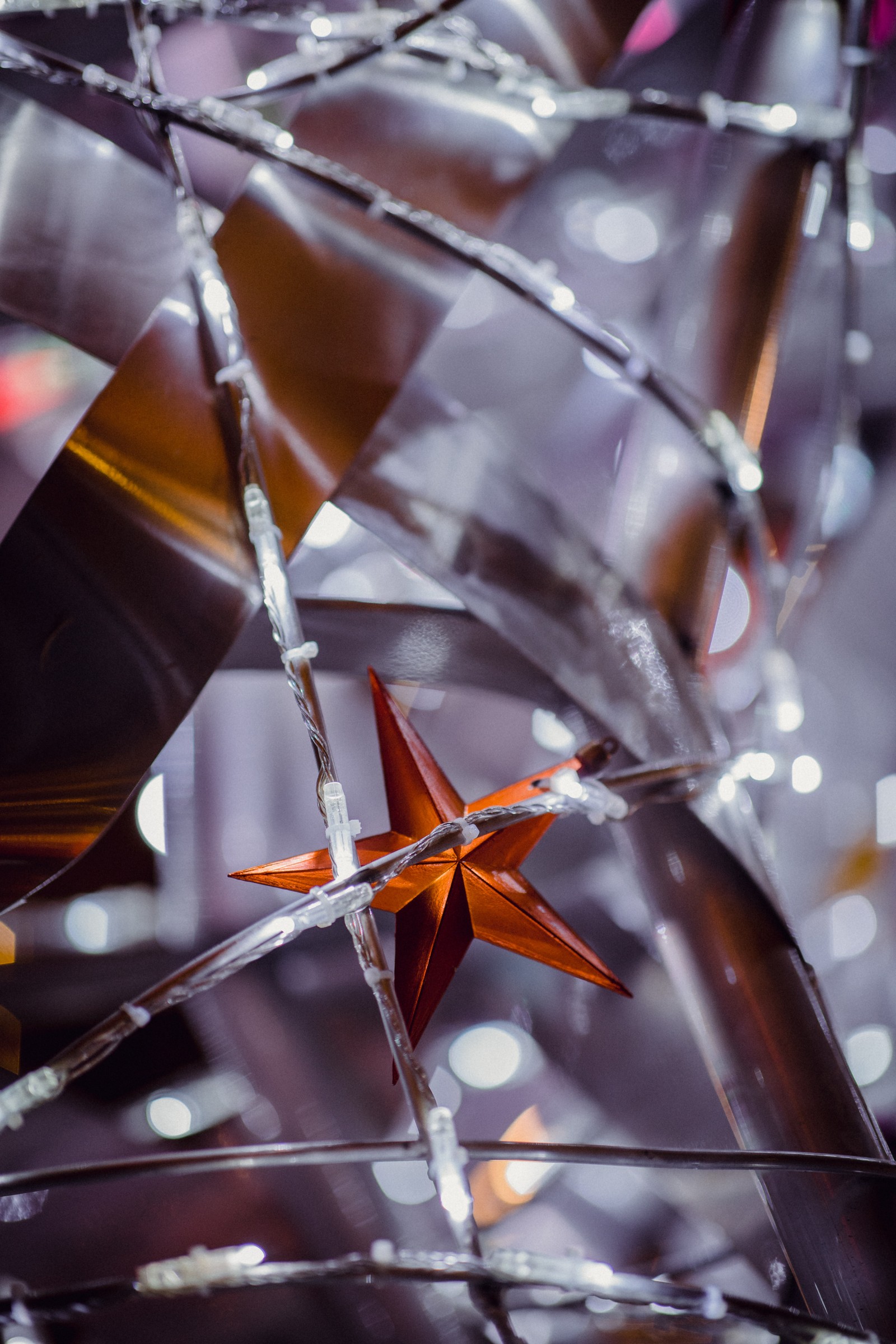 There is a paper star that is hanging from a wire (garland, branch, new year, metal, orange)