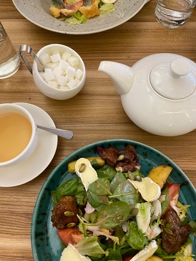 Ensalada vegetariana vibrante servida en un tazón de cerámica junto a una tetera y cubos de azúcar sobre una mesa de madera.