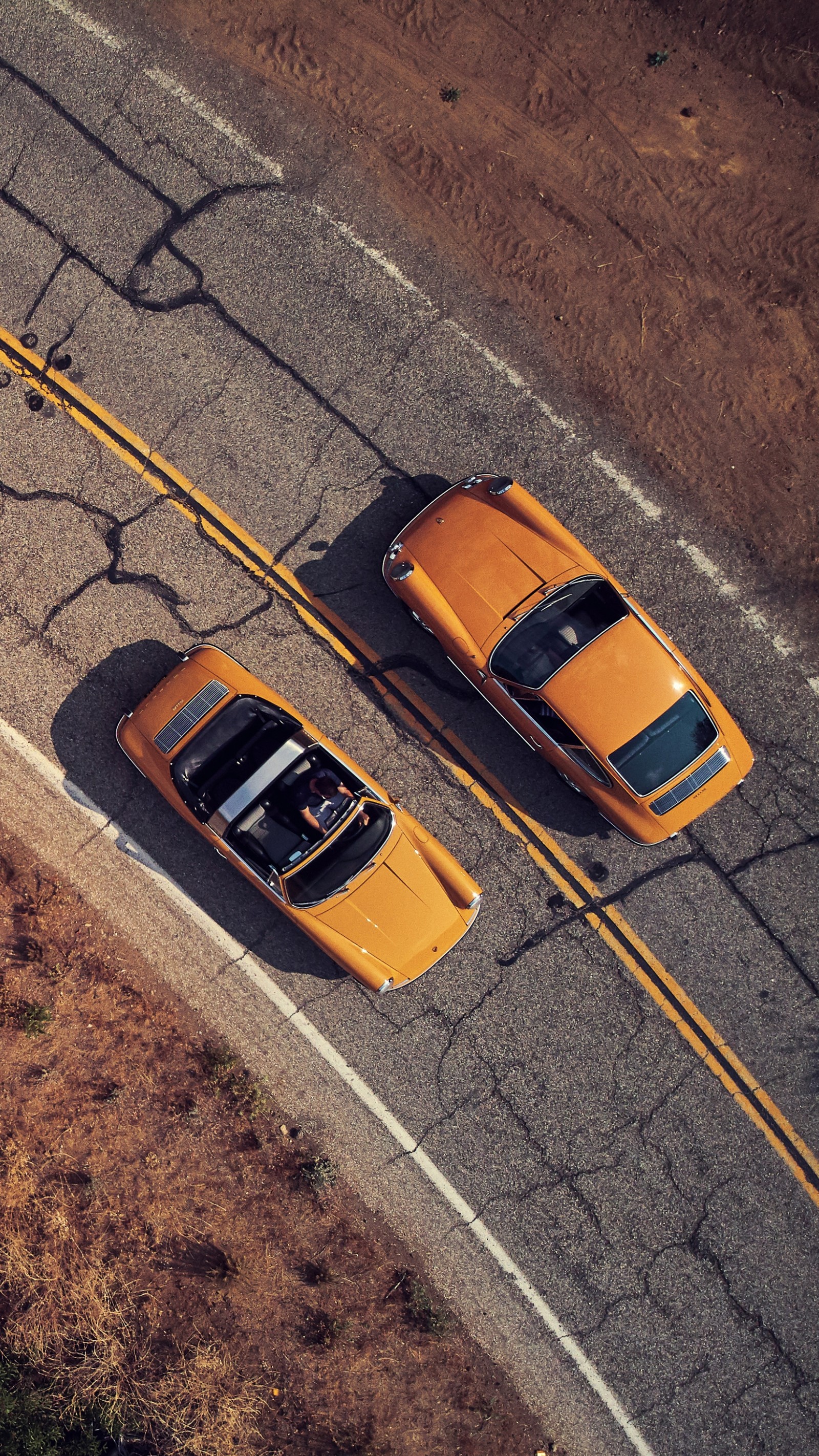 Two yellow cars are parked on the side of the road (cars, porsche, porsche 911, porsche cayman, sports car)