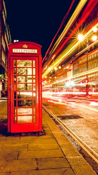 Cabina telefónica roja iluminada en medio del tráfico de la ciudad por la noche