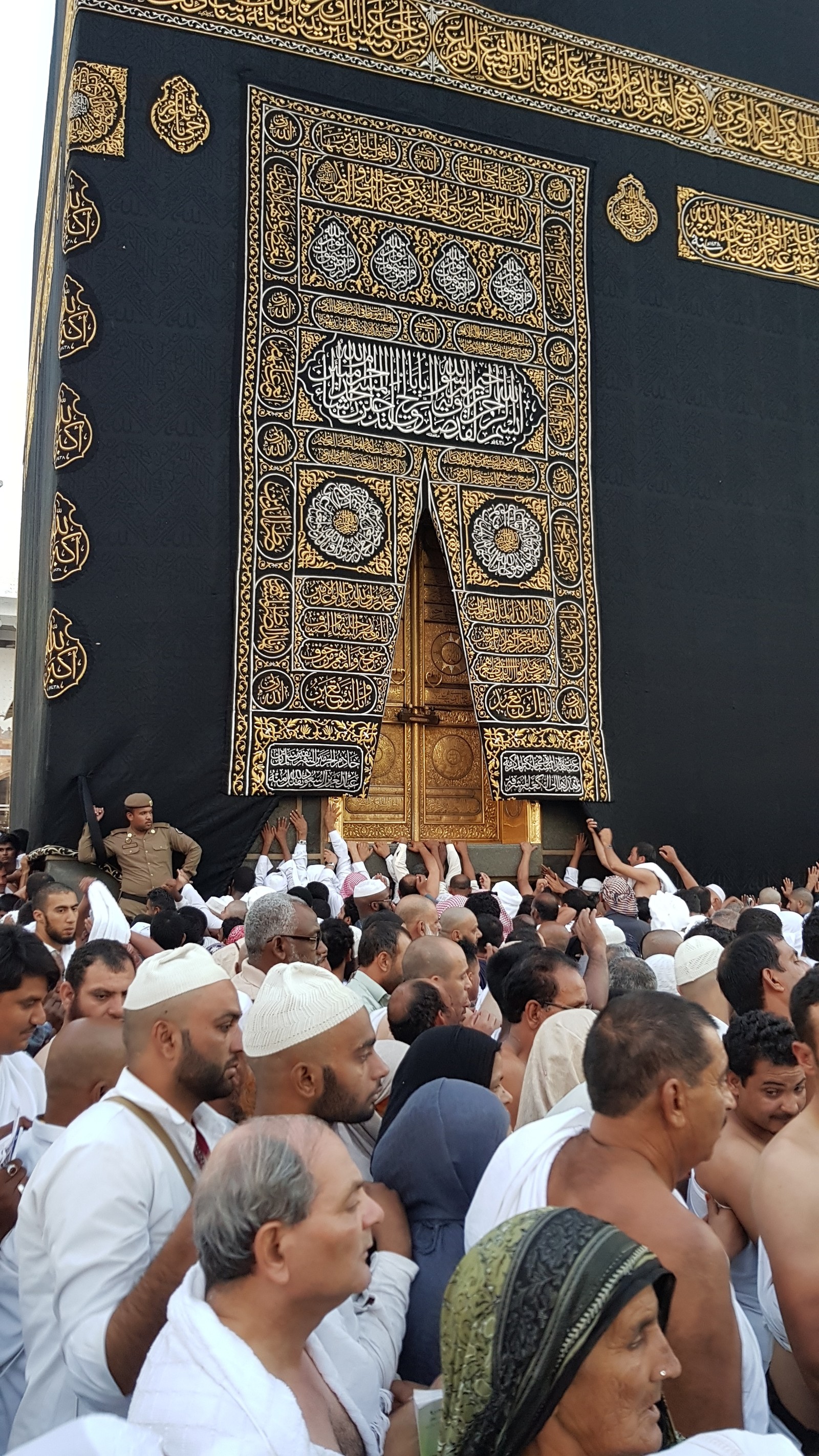 Eine menschenmenge, die um ein großes schwarzes gebäude steht (tür, heilig, islam, kabba, mekka)