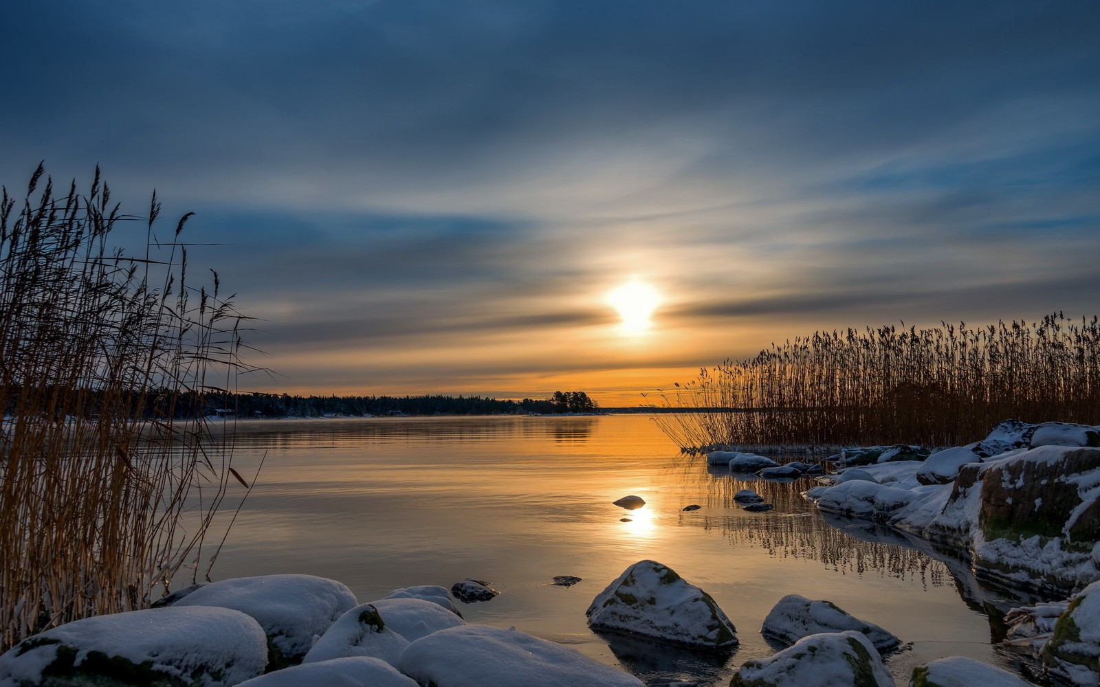 Um pôr do sol sobre um lago com pedras cobertas de neve e juncos (natureza, água, inverno, horizonte, nuvem)